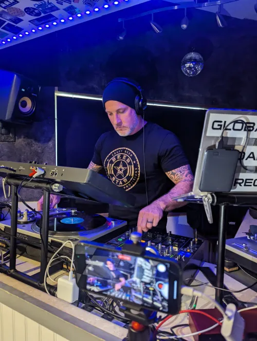 Phil Anthony performing live with turntables and mixer while streaming, lit by blue stage lighting