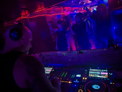 Phil Anthony performing at a nightclub with a crowd visible in the background, illuminated by red and blue lighting effects