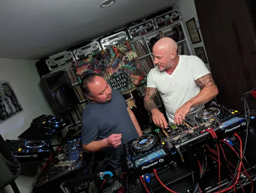 DJ smiling at camera while streaming, with mobile phone setup showing live feed