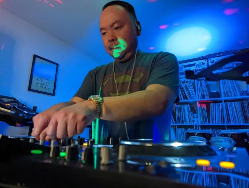 DJ performing with red lighting and crowd in background, focused on Pioneer mixer