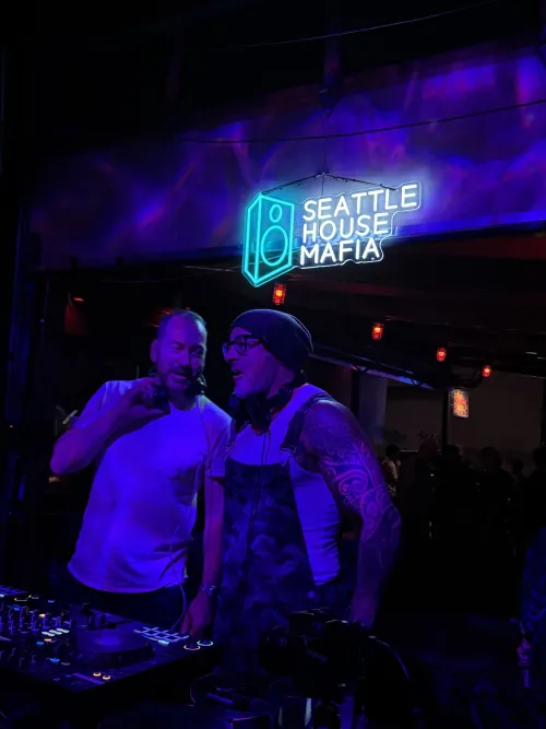 Two Seattle House Mafia DJs behind the decks under the Seattle House Mafia neon sign